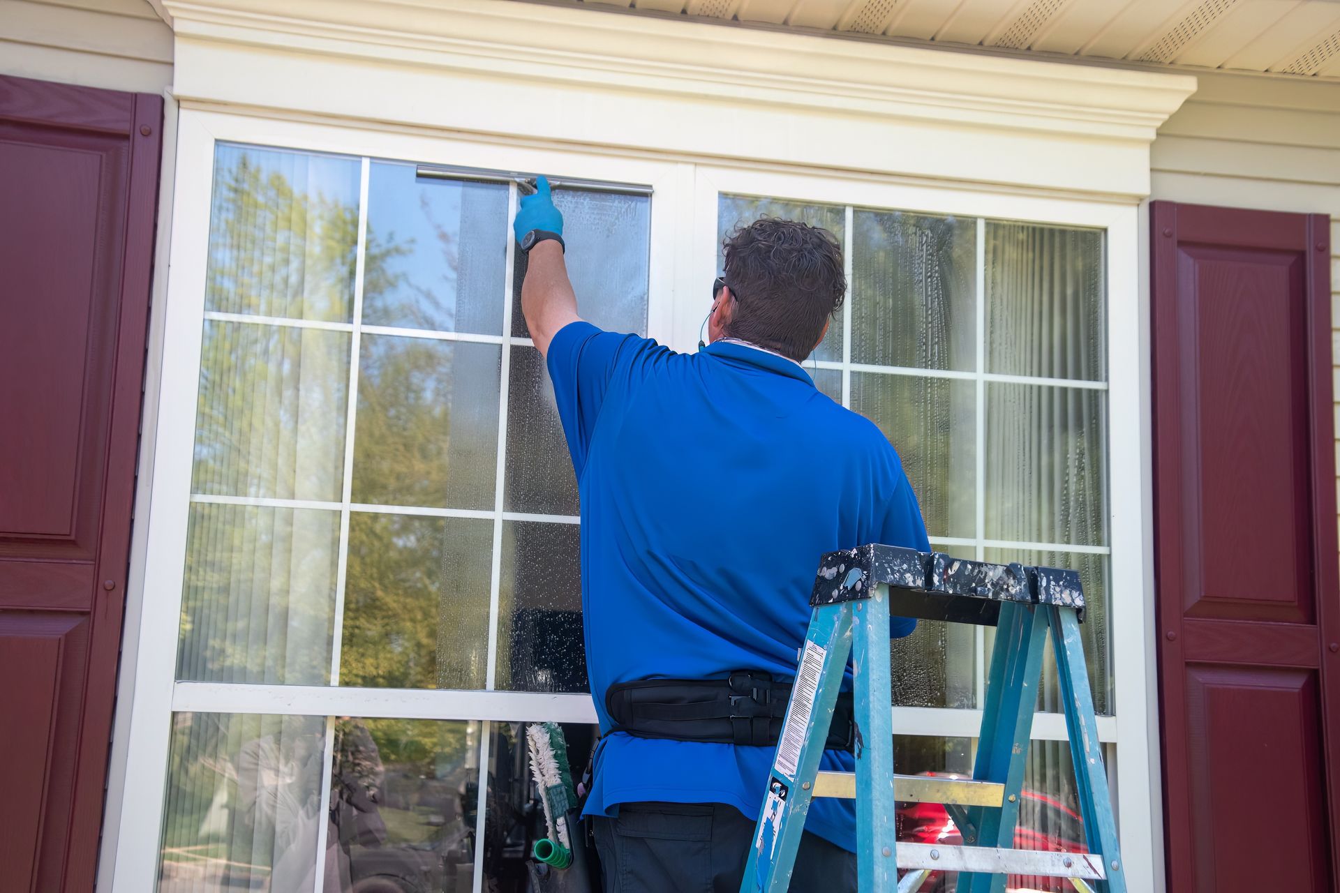 Person cleaning an upper-story window from a ladder beside a house