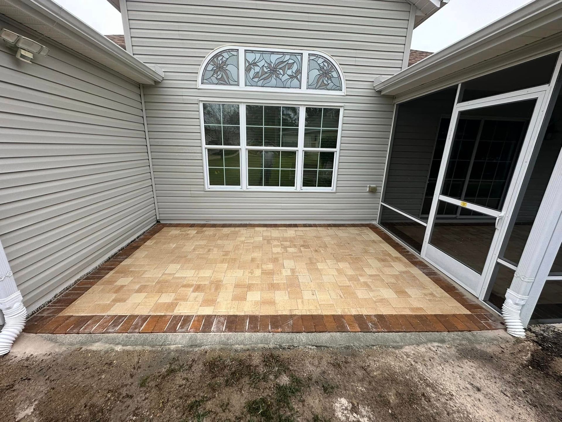 There is a patio in the backyard of a house with a screened in porch.