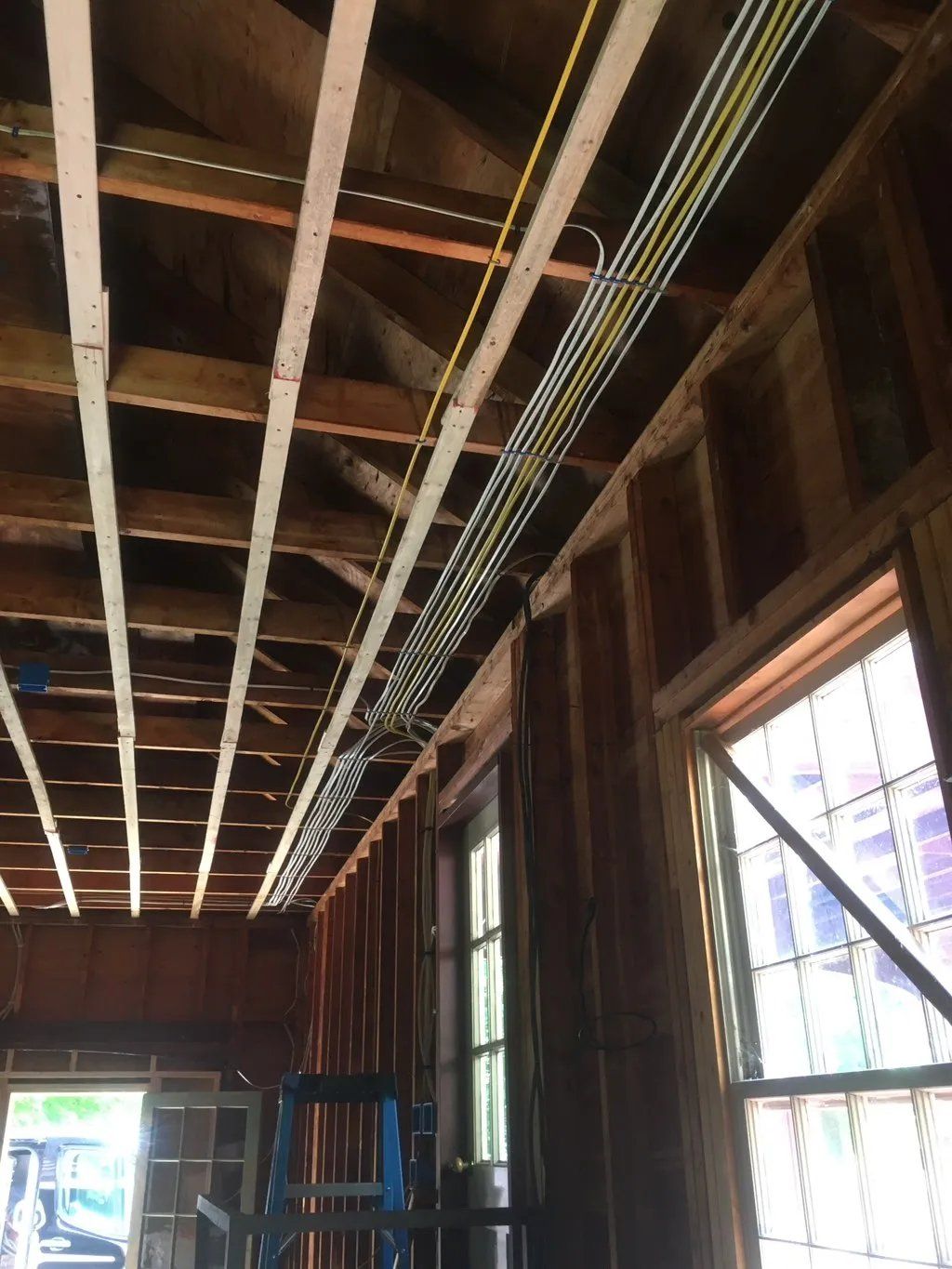 Electrical wiring runs along wooden ceiling beams in a room with windows.