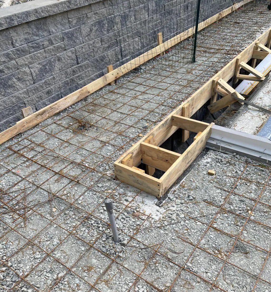 Construction site: Rebar grid laid over gravel base, wooden forms for concrete pour.