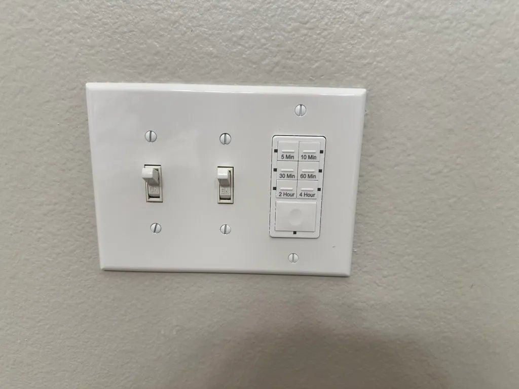 White wall plate with three switches: two toggle switches and a dimmer control with multiple buttons.