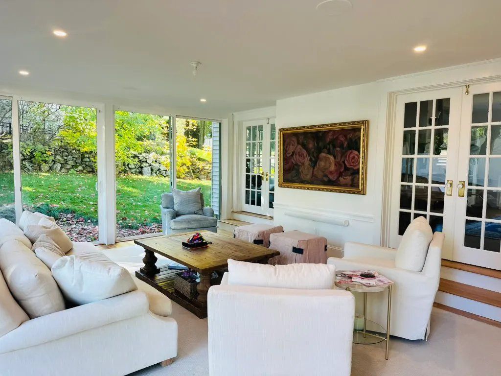 Sunroom with white furniture, glass walls, a garden view, and floral artwork.