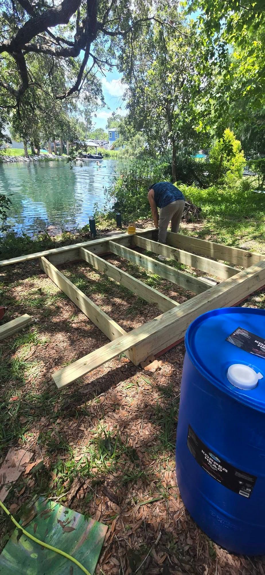 A man is working on a wooden deck next to a blue barrel.