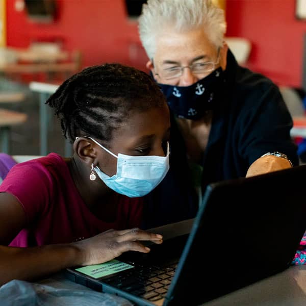An adult assists youth on a laptop