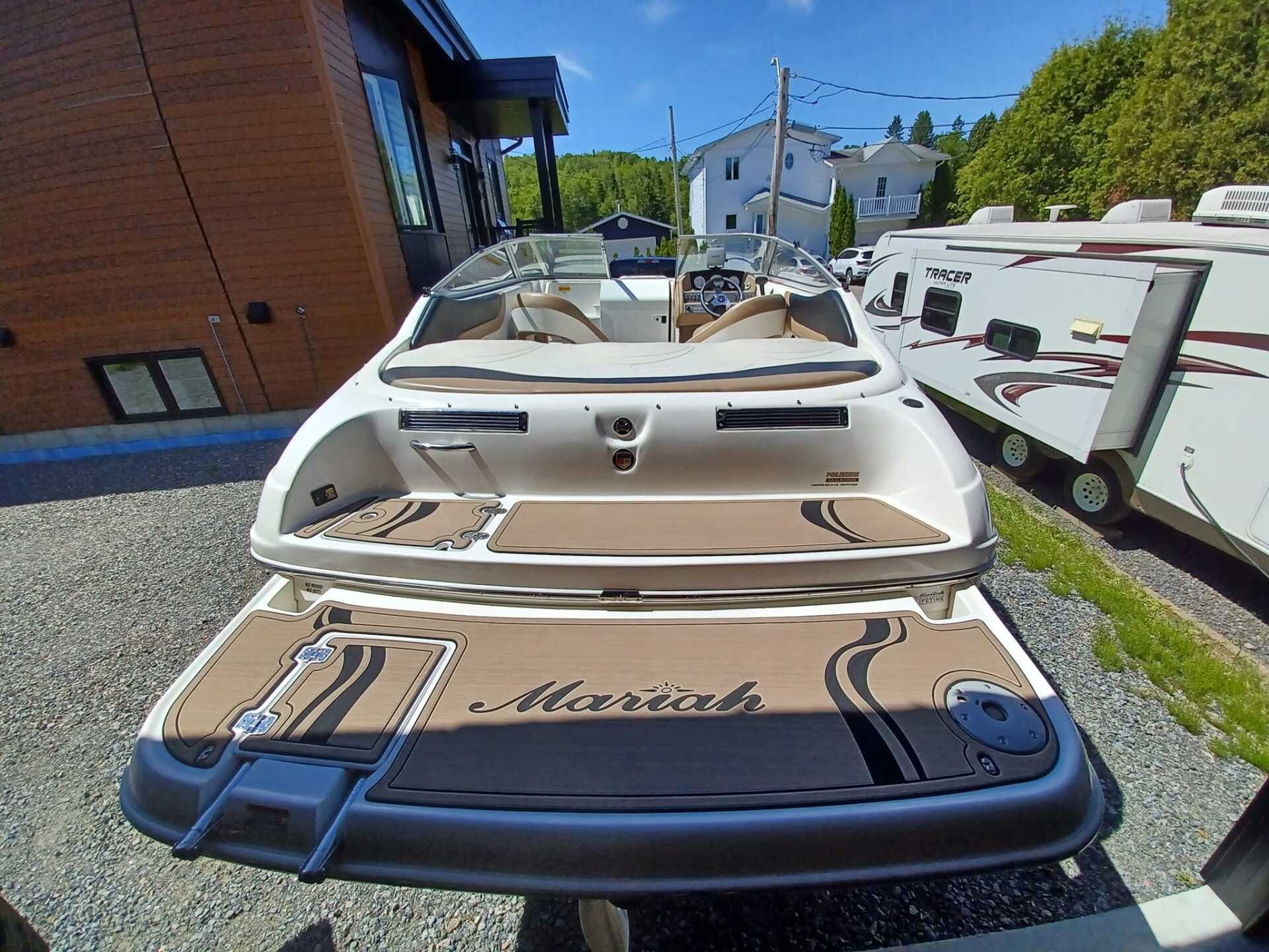 Bateau à moteur blanc et beige sur gravier, vue extérieure, avec plateforme de baignade ouverte.