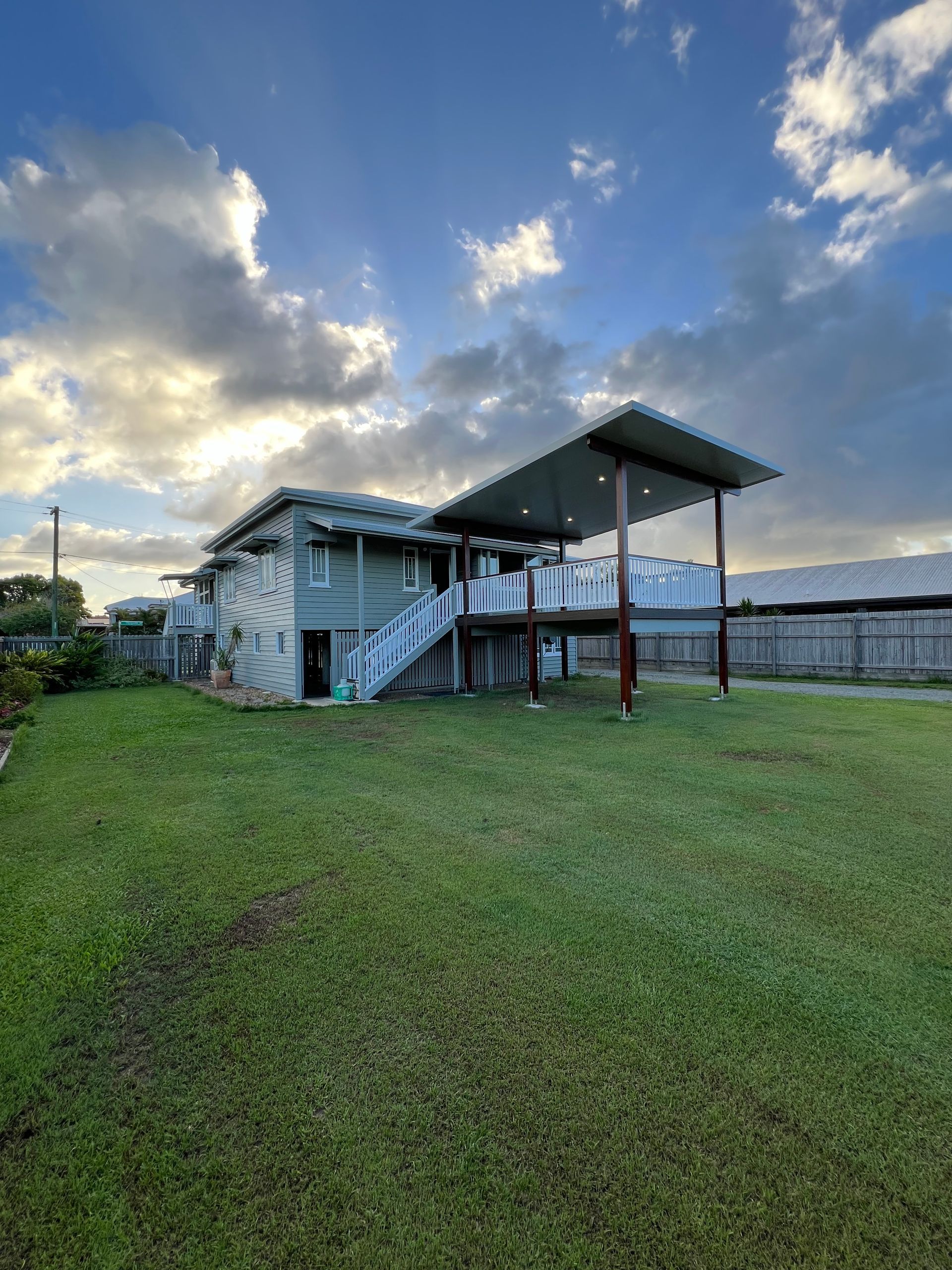 Elevated timber deck with insulated roof patio cover on steel posts, attached to a raised Queenslander-style home overlooking a landscaped backyard