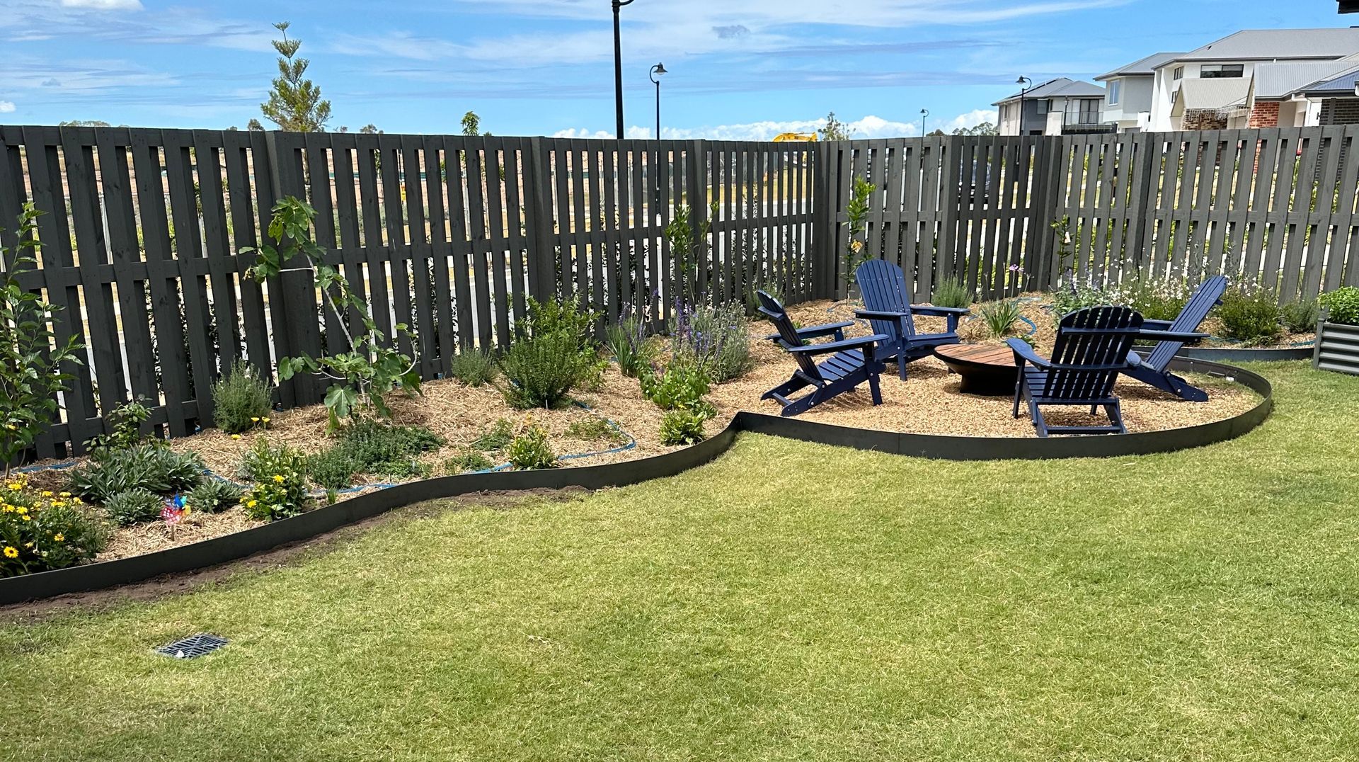 Curved Straightcurve garden edging separating mulched garden beds and a gravel seating area from new turf, with an outdoor fire pit and chairs