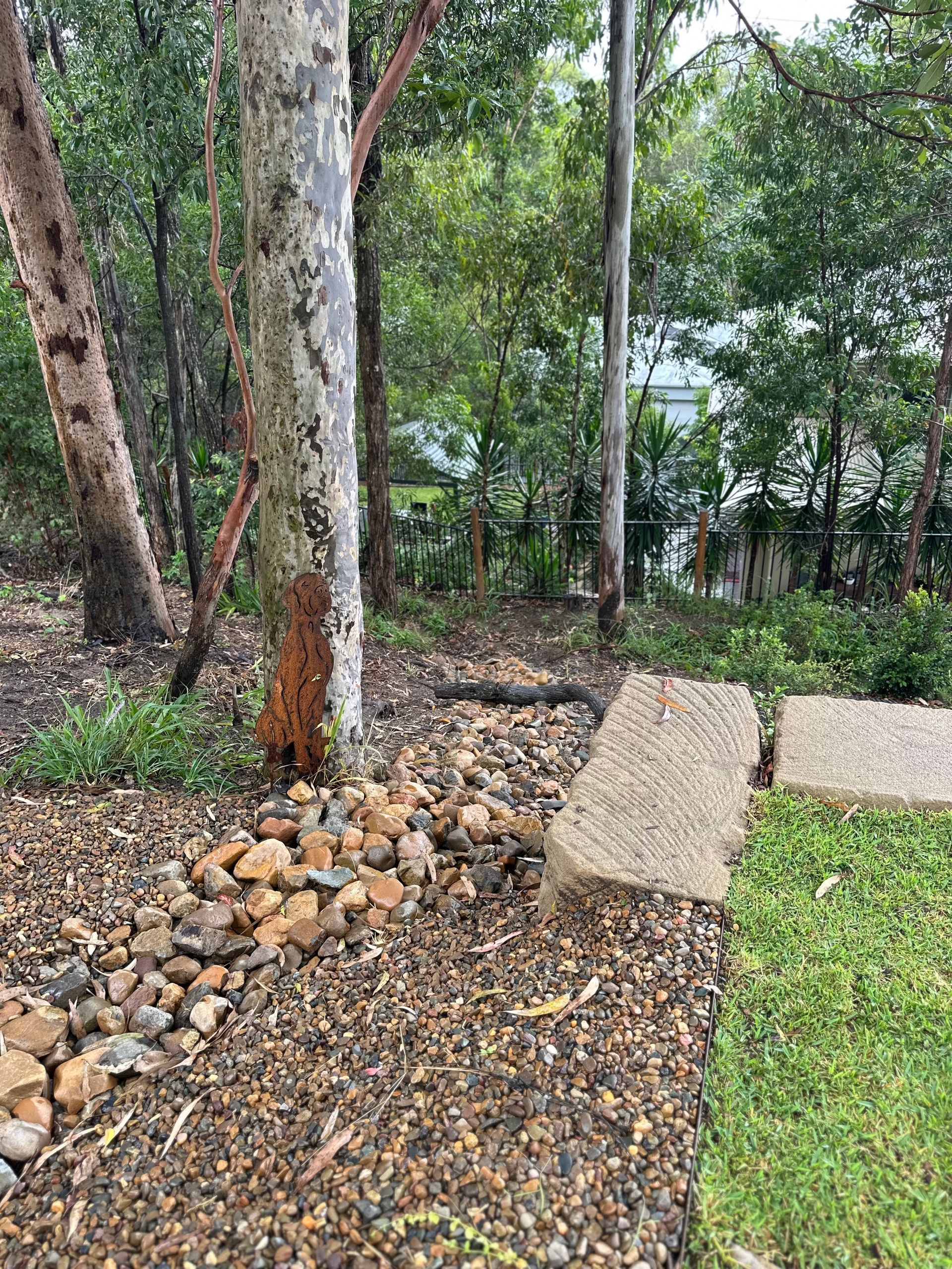 River pebble drainage bed around a native gum tree, with sandstone blocks set into a naturalistic garden setting