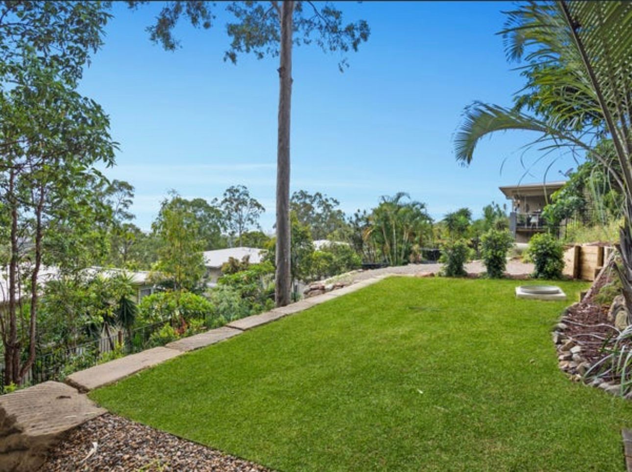 Freshly laid turf lawn with sandstone block retaining wall, gravel border and rock retaining edge, part of a landscaped Gold Coast backyard with hinterland views
