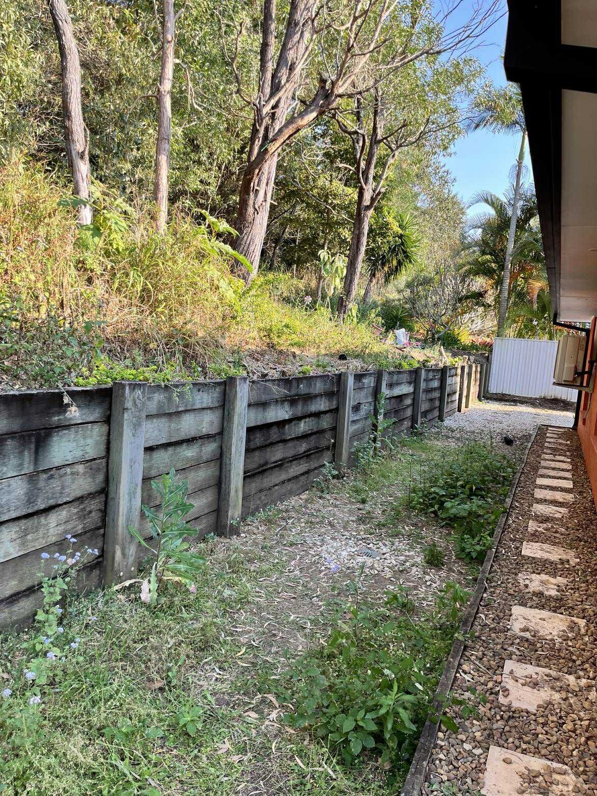 Before and after comparison of a timber retaining wall rebuild, from rotting sleepers to a new wall with turf