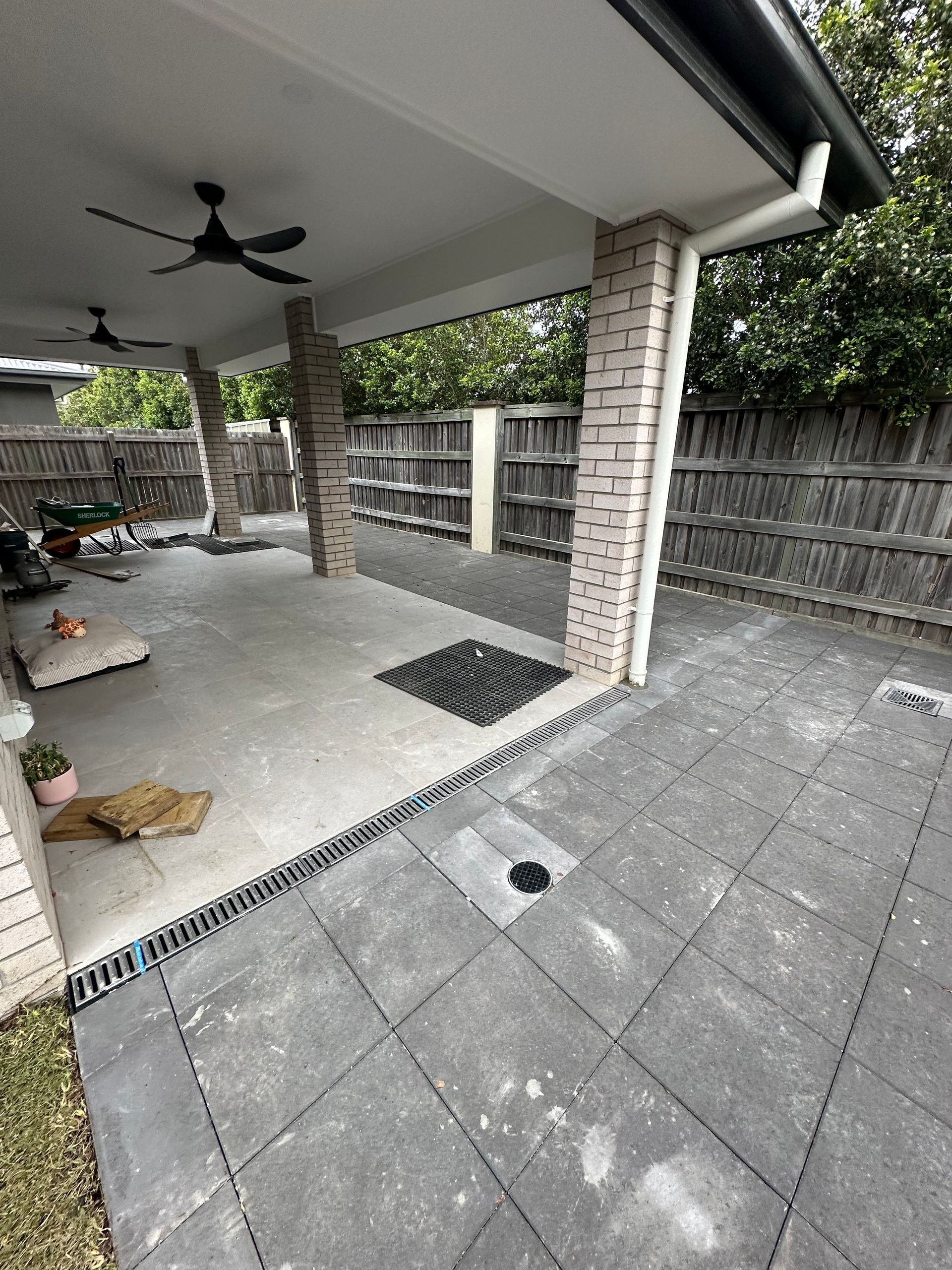 Linear channel drain running along the edge of a covered patio, separating tiled outdoor areas of different levels