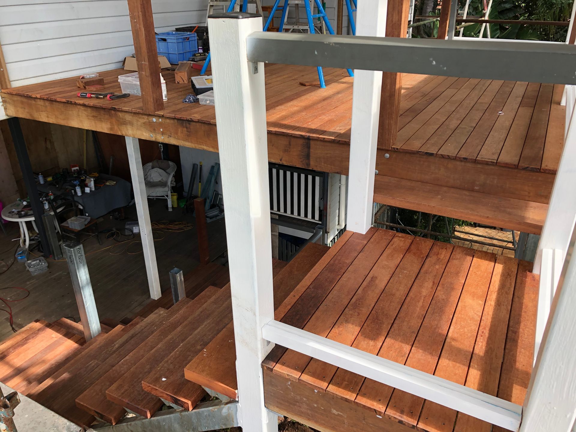 Multi-level hardwood timber deck with white balustrade posts and connecting staircase, under construction on an elevated Queenslander home