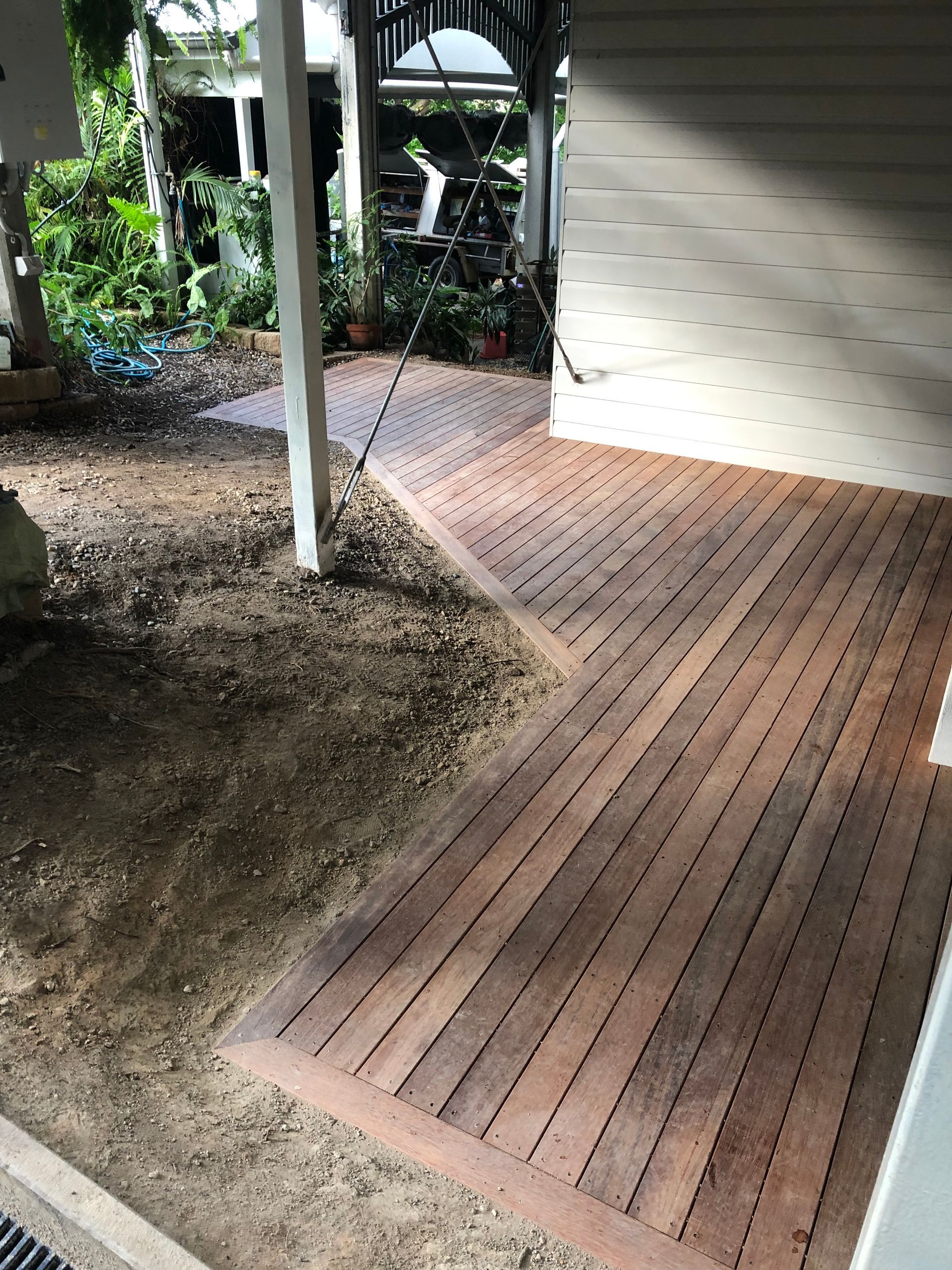 Hardwood timber deck with picture-frame border under a covered carport, freshly built beside bare soil ready for landscaping
