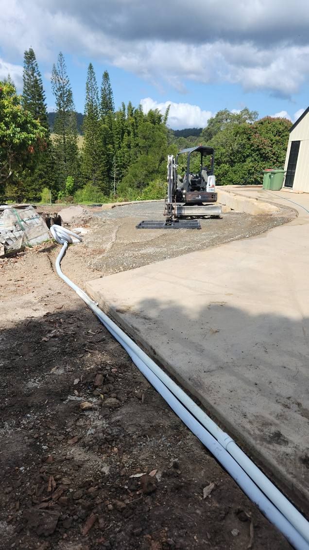 PVC stormwater drainage pipes running along a concrete slab edge, with excavator preparing the site in the background