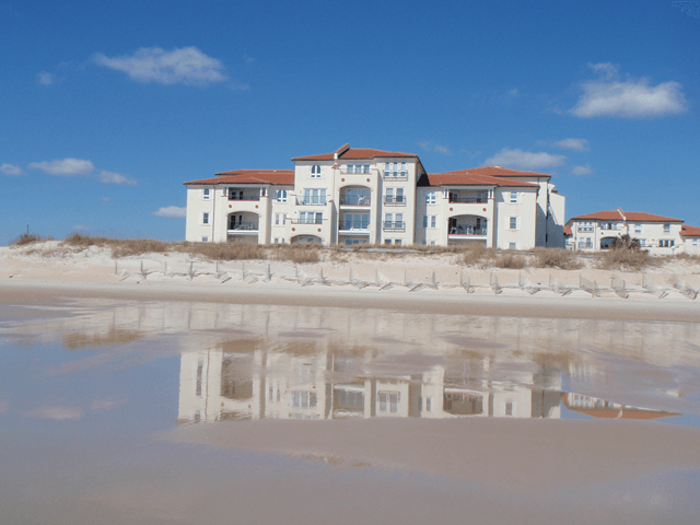 A large white building sits on top of a sandy beach