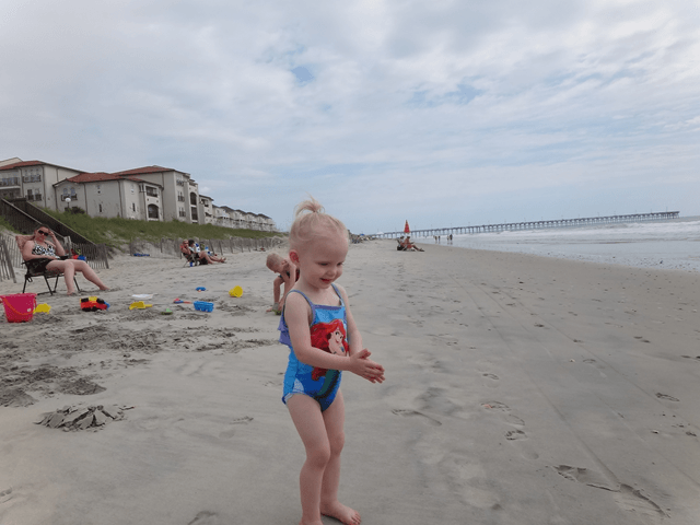 A little girl in a blue bathing suit is standing on a beach