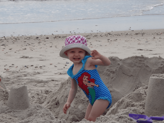 A little girl in a mermaid swimsuit is playing in the sand