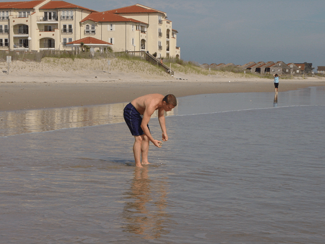 A man is bending over in the water on a beach