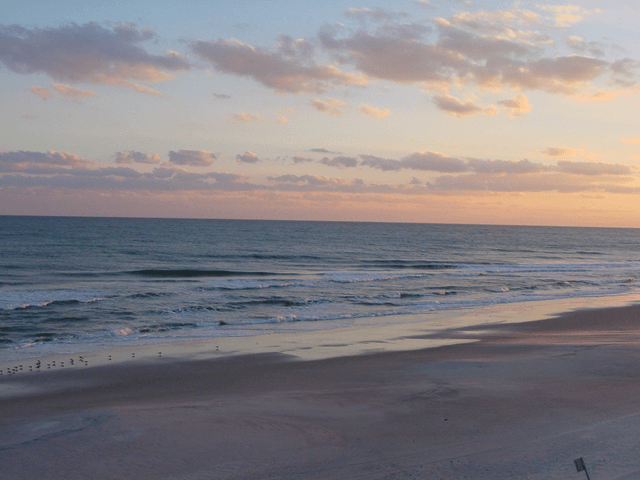 A beach at sunset with a chair in the foreground
