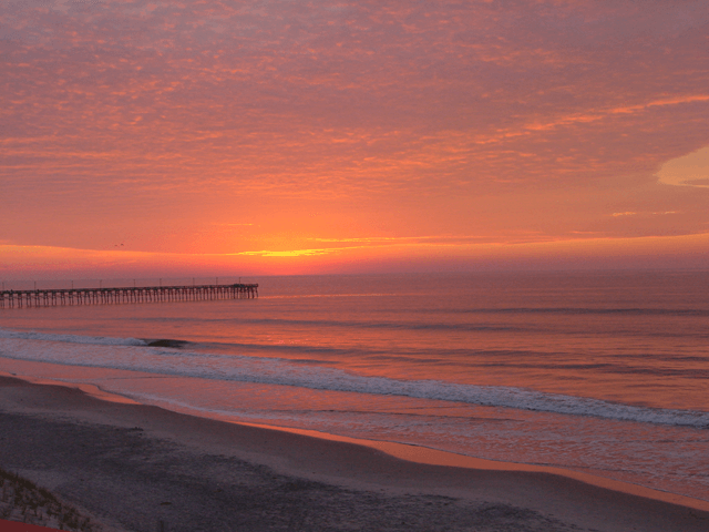 A sunset over a beach with a pier in the background