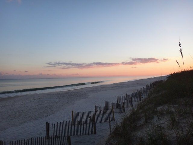 A sunset over a beach with a fence in the foreground