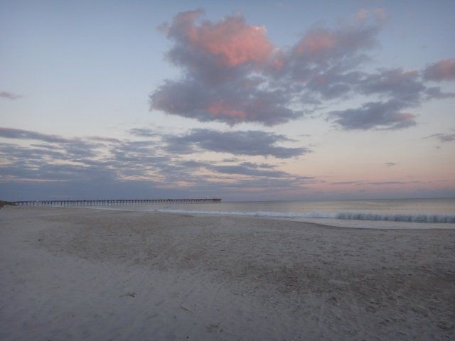 A beach at sunset with a pier in the distance