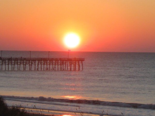 The sun is setting over the ocean with a pier in the foreground