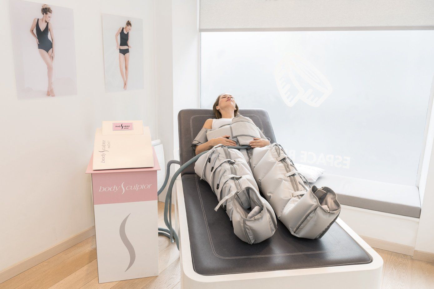 Eine Person liegt in einem hellen Klinikzimmer auf einer Behandlungsliege und trägt graue Kompressionsstiefel.