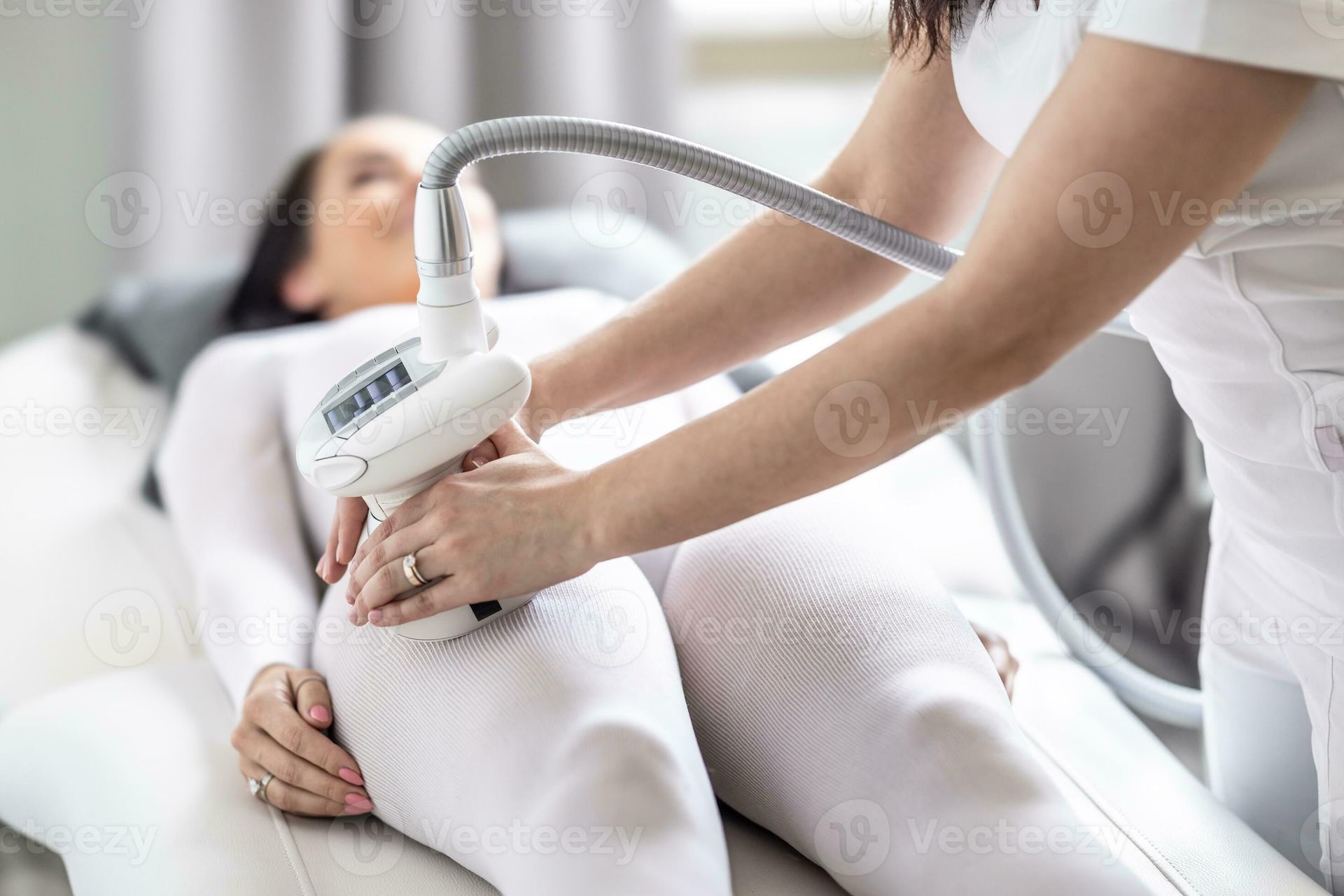 Spa-Therapeutin verwendet ein handgeführtes Körperbehandlungsgerät an einer in weiße Handtücher gehüllten Kundin.