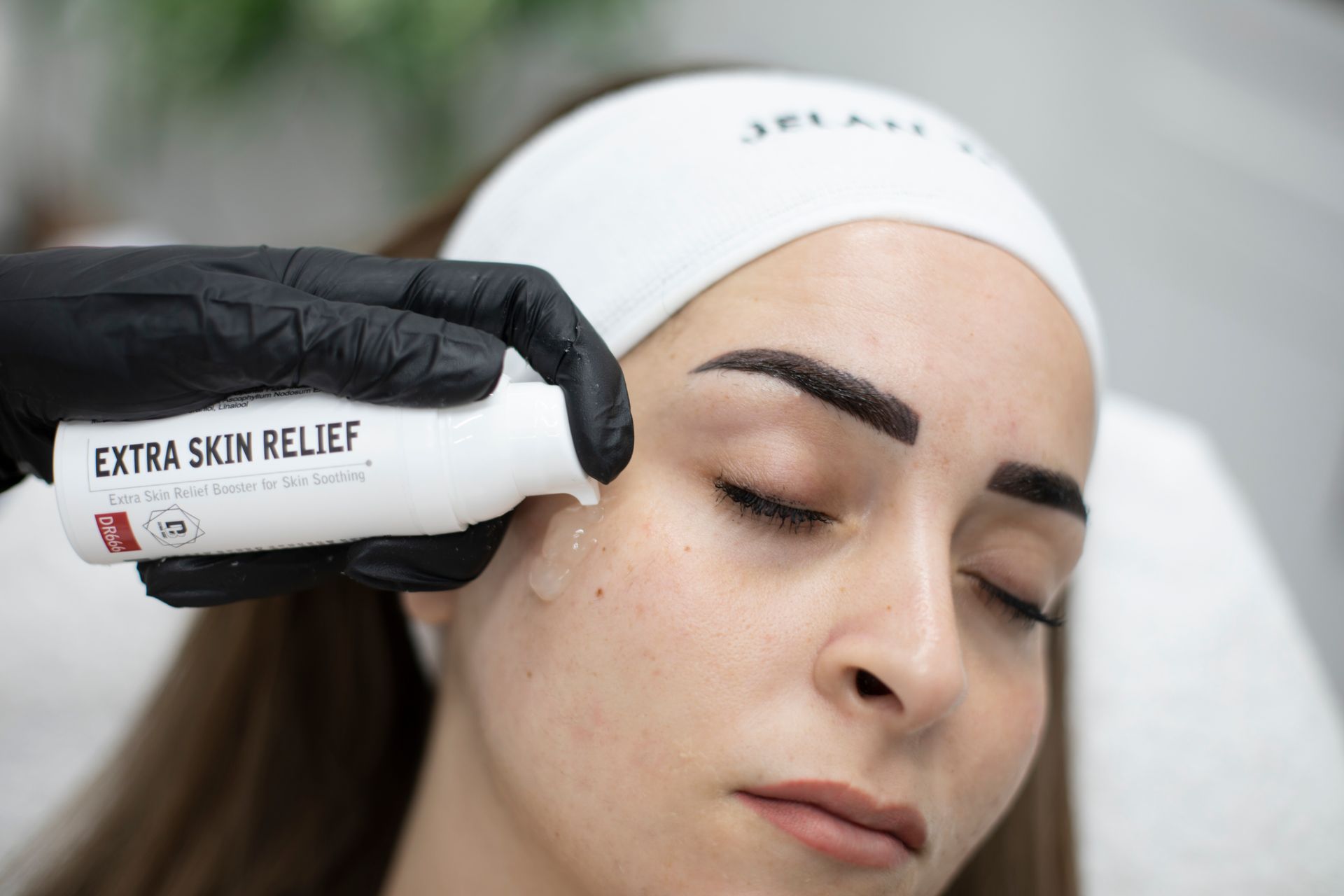 Eine behandschuhte Hand legt einem Menschen, der mit geschlossenen Augen liegt, ein Extra Skin Relief-Gerät an die Schläfe.
