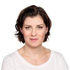 Porträt einer Frau mit kurzen dunklen Haaren, die ein weißes Oberteil trägt, vor einem schlichten weißen Hintergrund