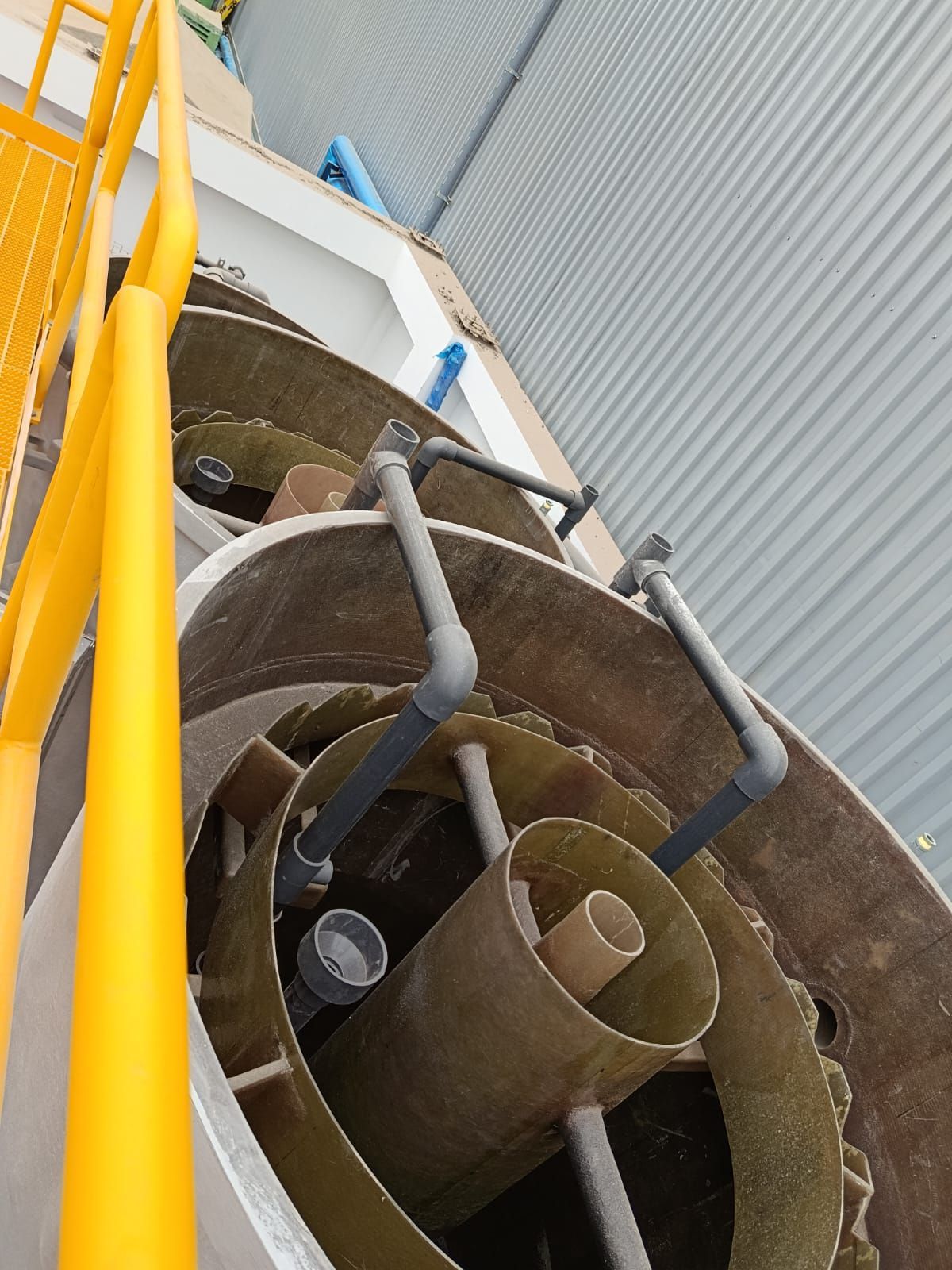 Conductos y tuberías metálicas industriales junto a una barandilla amarilla en una plataforma de escalera.