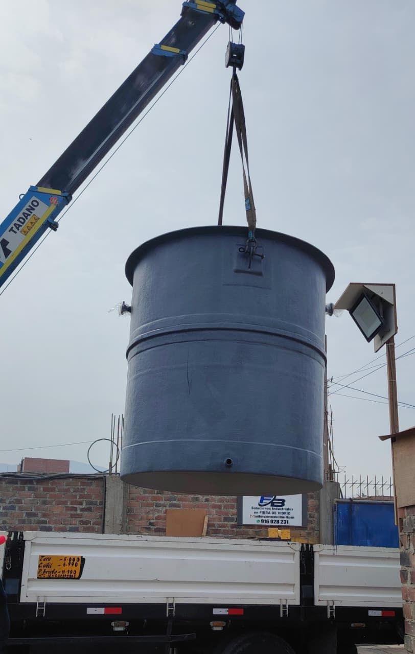 Una grúa eleva un gran tanque cilíndrico azul sobre un camión de plataforma en una obra de construcción.