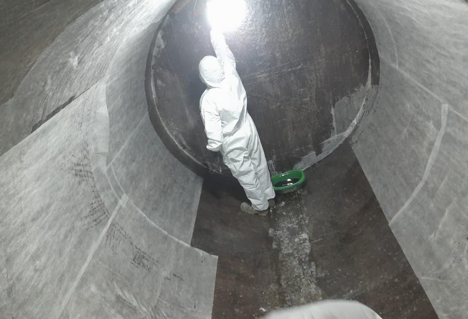 Un trabajador con un traje protector blanco se encuentra dentro de una gran tubería de hormigón