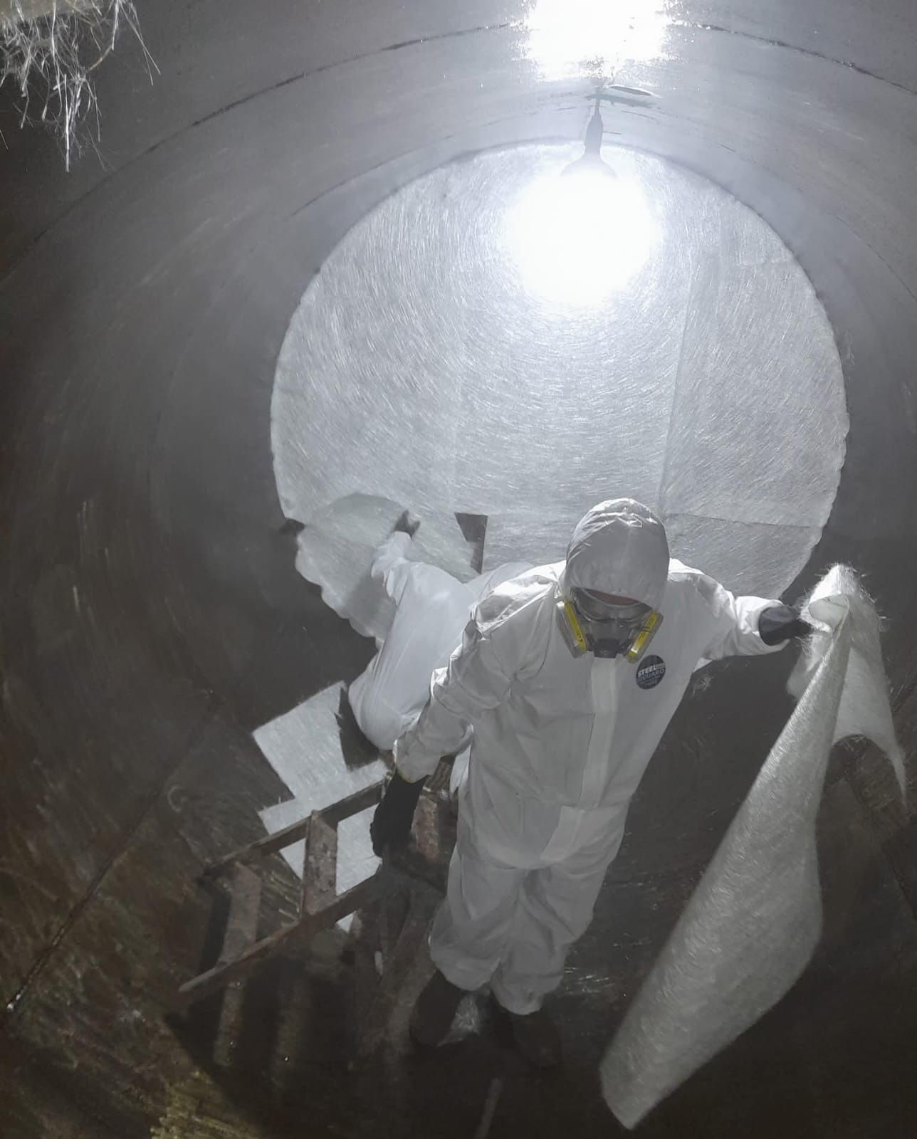 Un trabajador con un traje protector blanco sube unas escaleras dentro de un gran tanque o tubería industrial.