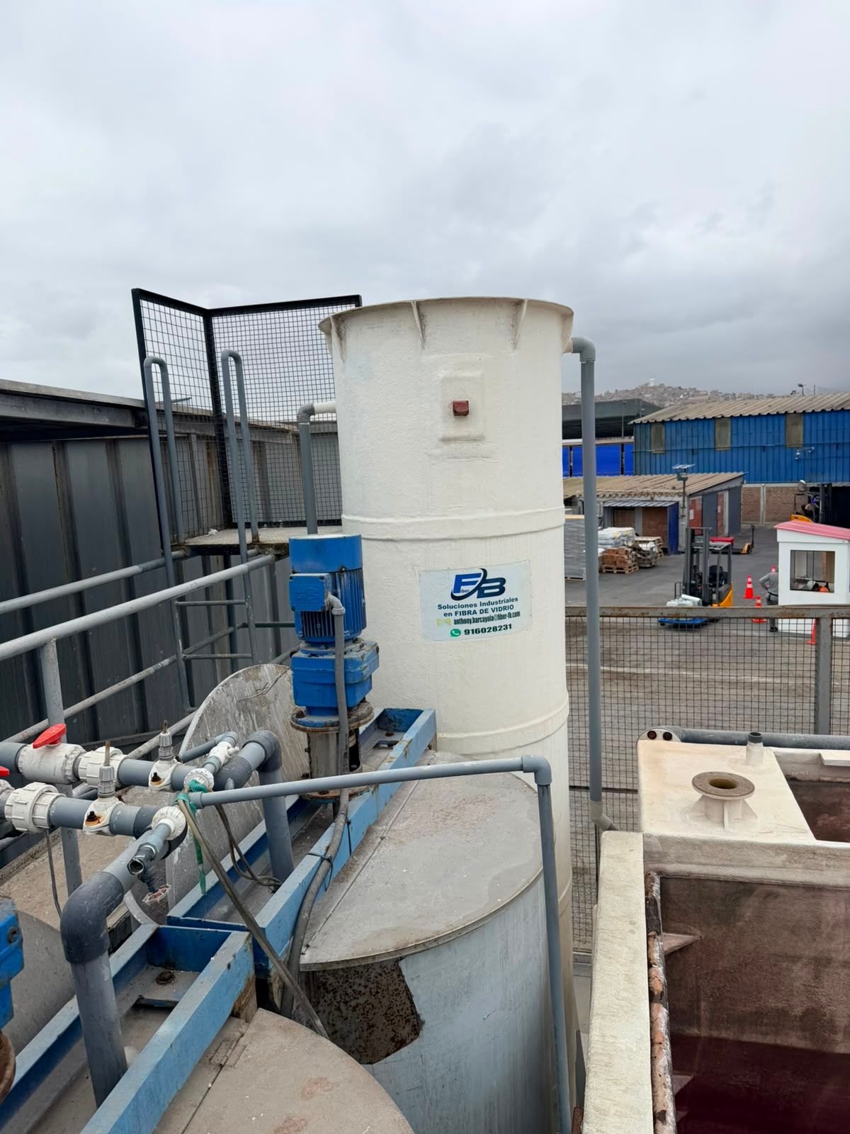 Sitio industrial con tanque de agua blanco, tuberías azules y cielo nublado en una plataforma en la azotea.