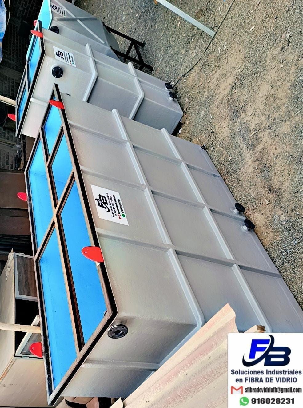 Gran máquina industrial gris con paneles azules y manijas rojas en un terreno de grava.