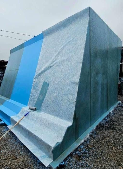 Gran estructura cubierta con una lona de color azul grisáceo, situada al aire libre sobre grava y sujeta con cuerdas.
