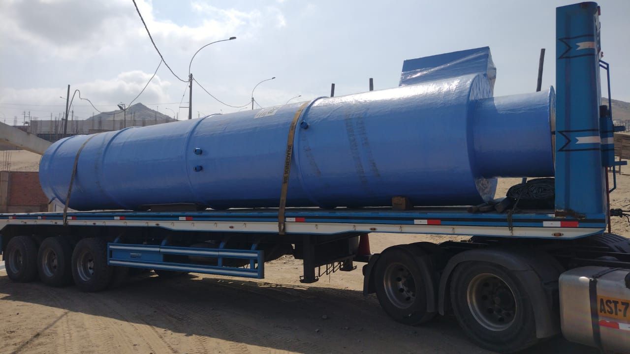 Tanque cilíndrico industrial azul sobre un remolque de plataforma estacionado al aire libre cerca de una carretera.