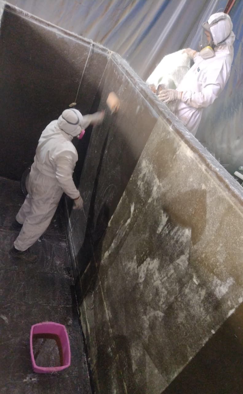Unos trabajadores con trajes protectores blancos limpian una gran pared