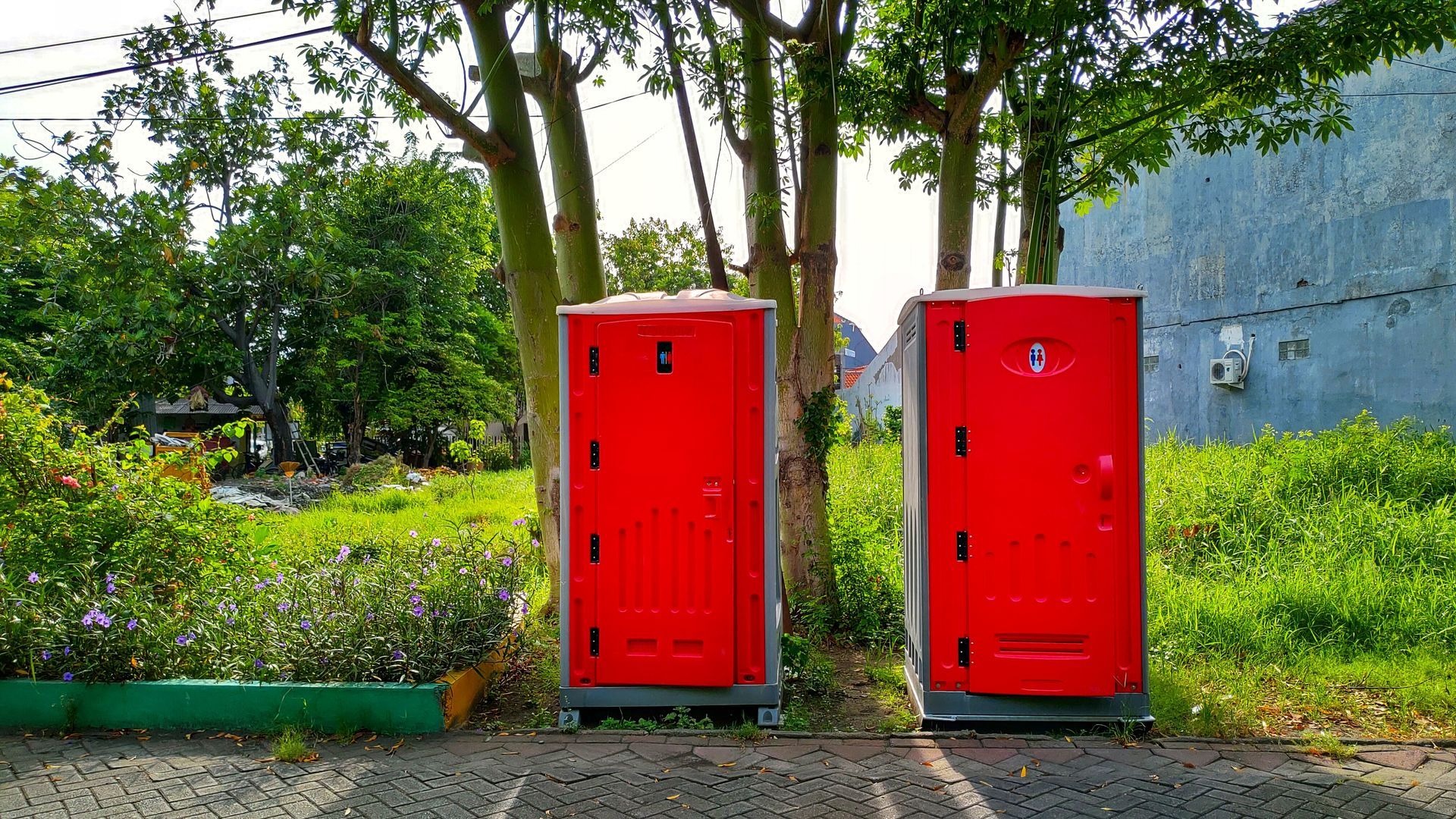 Red portable toilets on ground, with a forest background, representing portable toilets hires. Red portable toilets on ground, with a forest background, representing portable toilets hires.