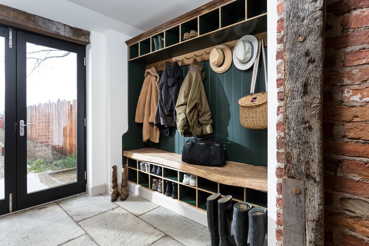 Mudroom with coat rack, shoe storage, and bench. Emerald green wall, wooden accents, brick and stone flooring.