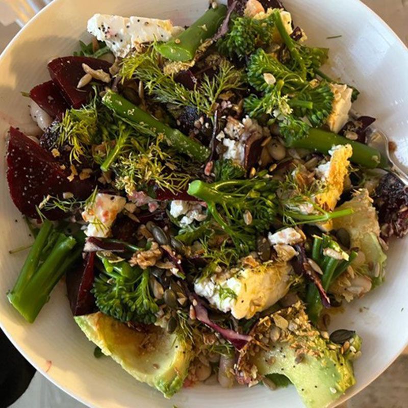 Salad bowl with avocado, beets, broccoli, feta, herbs, and seeds.