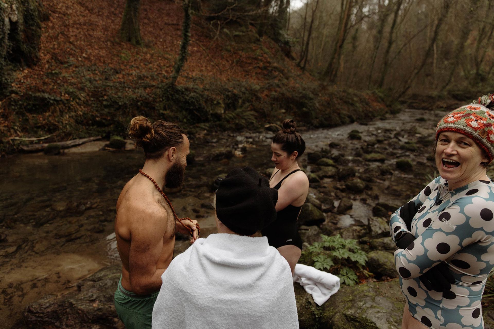 People in swimwear standing in a shallow river, surrounded by trees. One person has a surprised expression.