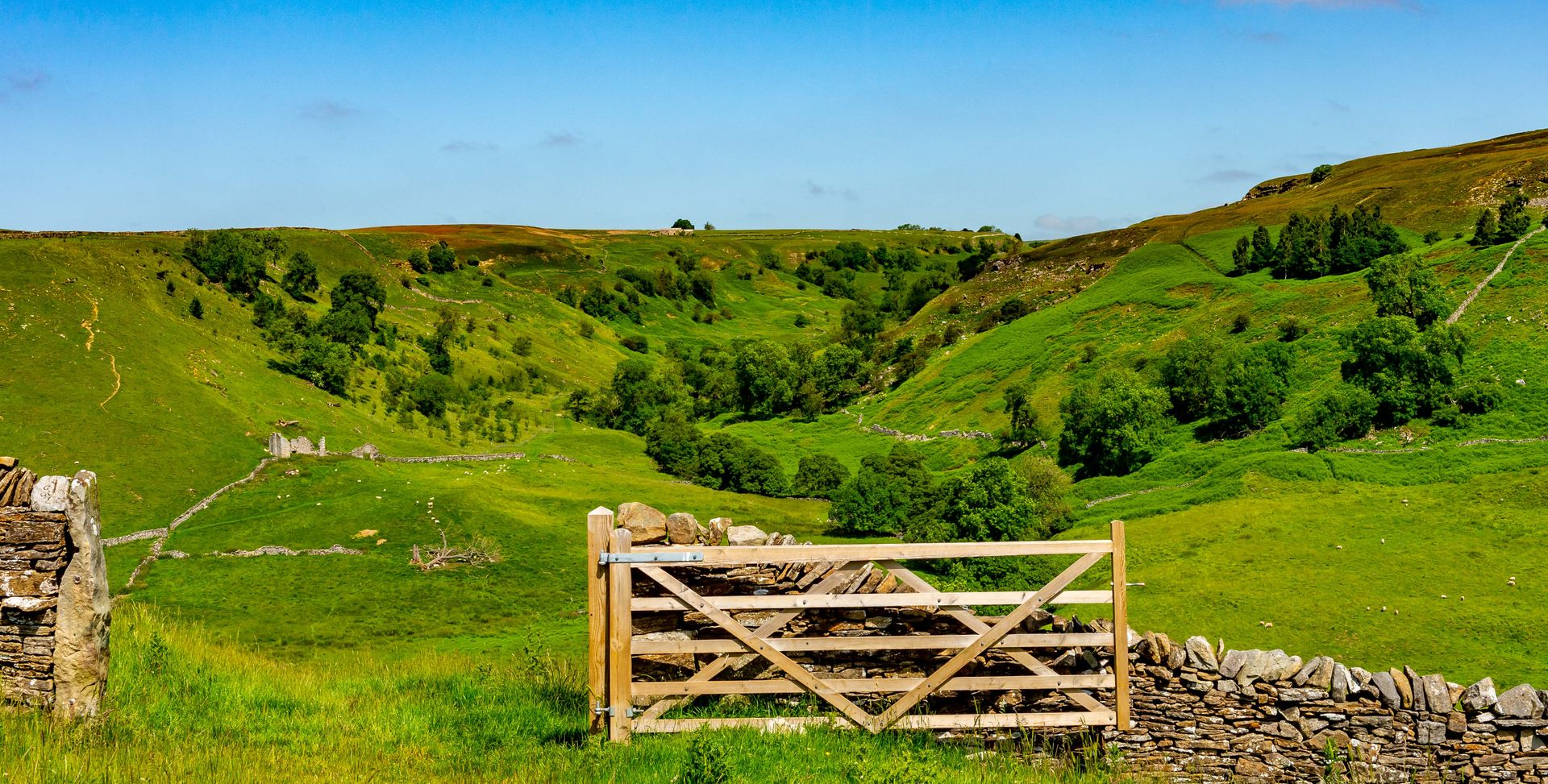 Wooden gate in lush green valley with rolling hills, blue sky.