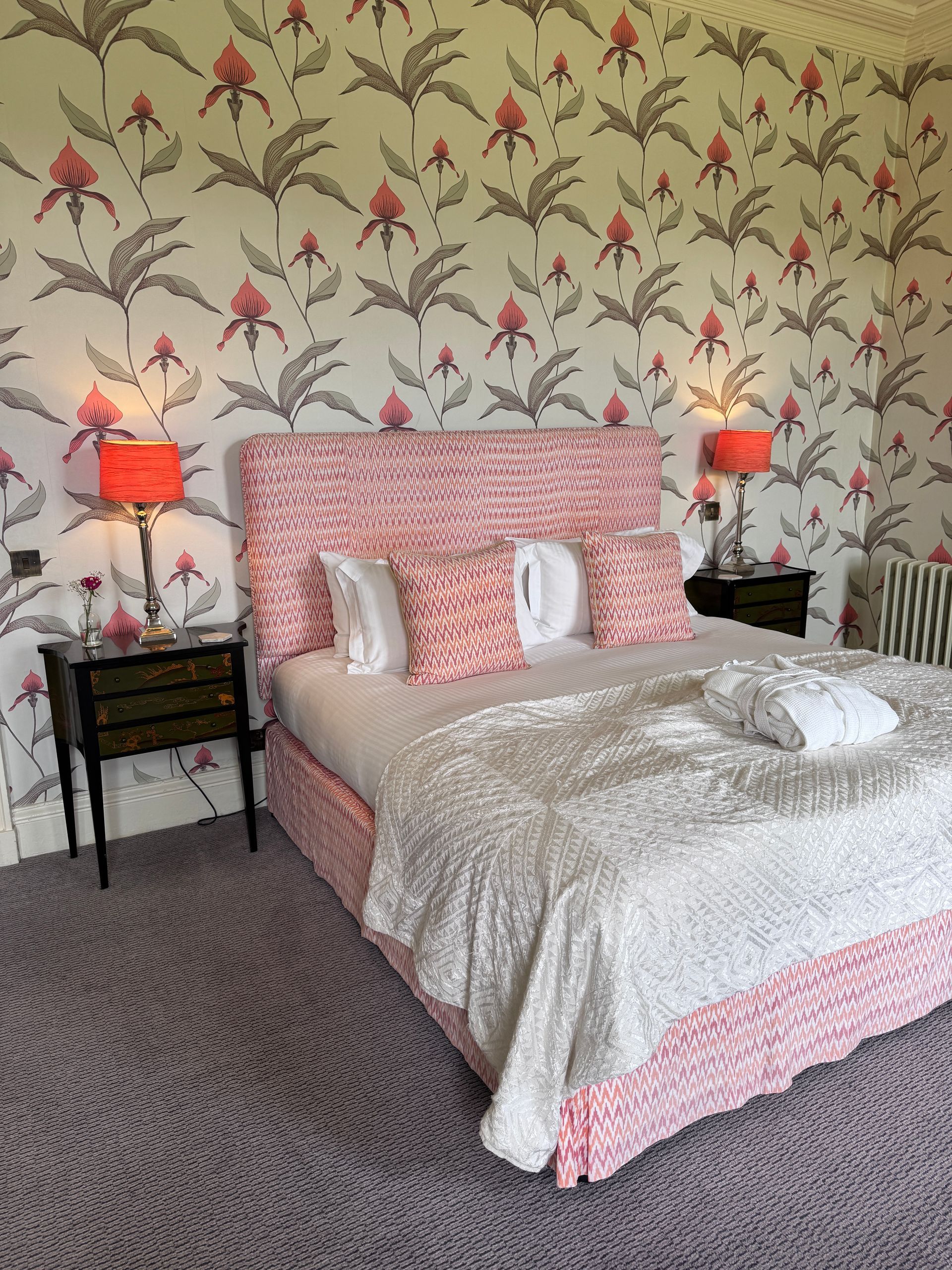 A bright, bedroom with king bed, cushions and bed side tables with orange lamps