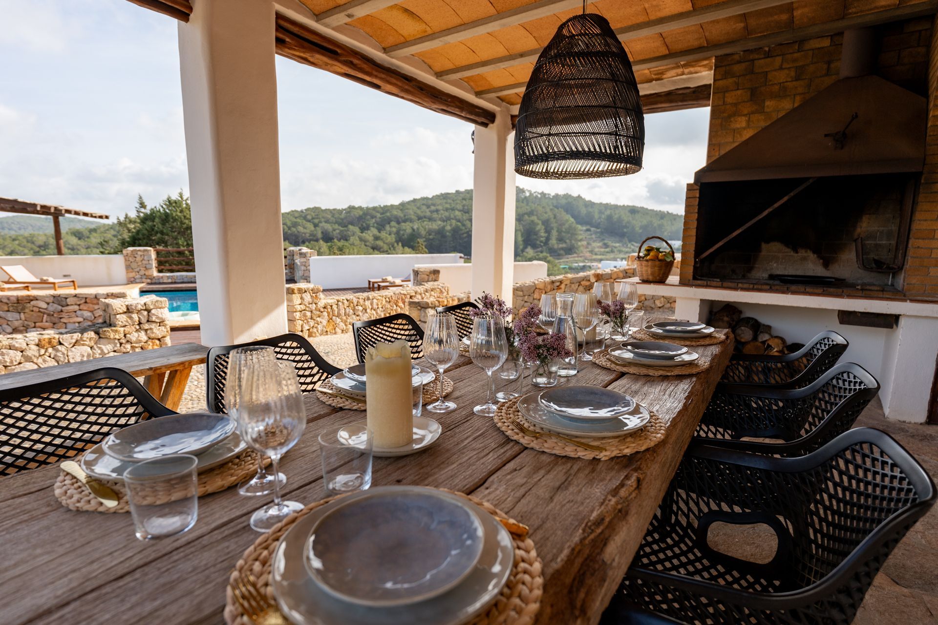 Outdoor dining table set for a meal, under a patio roof, with a mountain view.