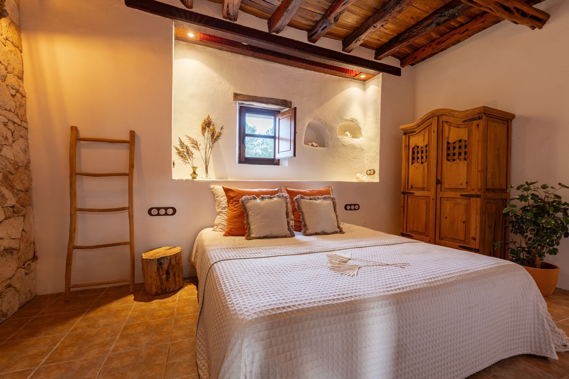 Bedroom with white walls, a wooden wardrobe, a bed with cream bedding, and a small window.