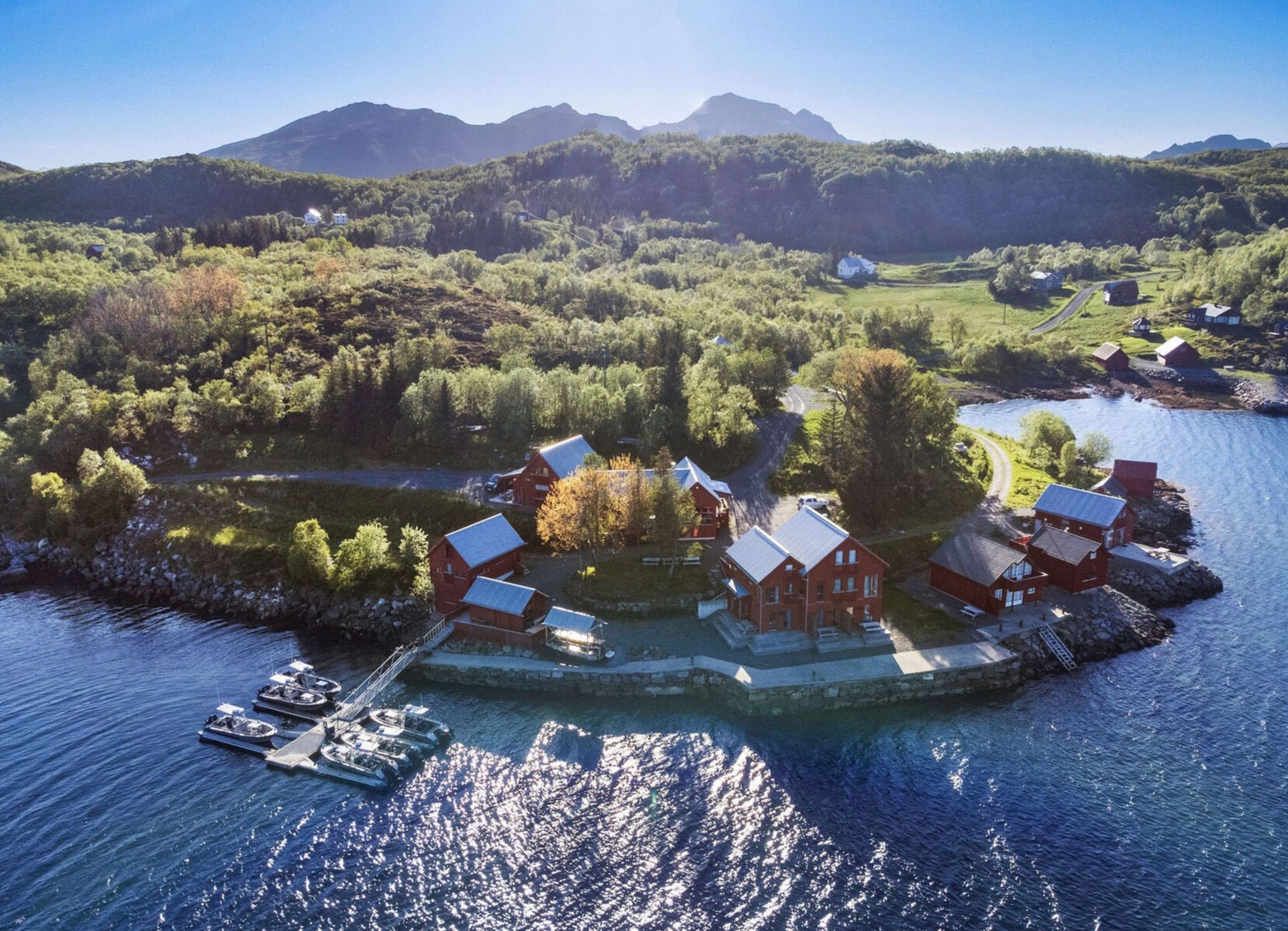 Coastal village with white buildings, boats, and calm water under a blue sky.