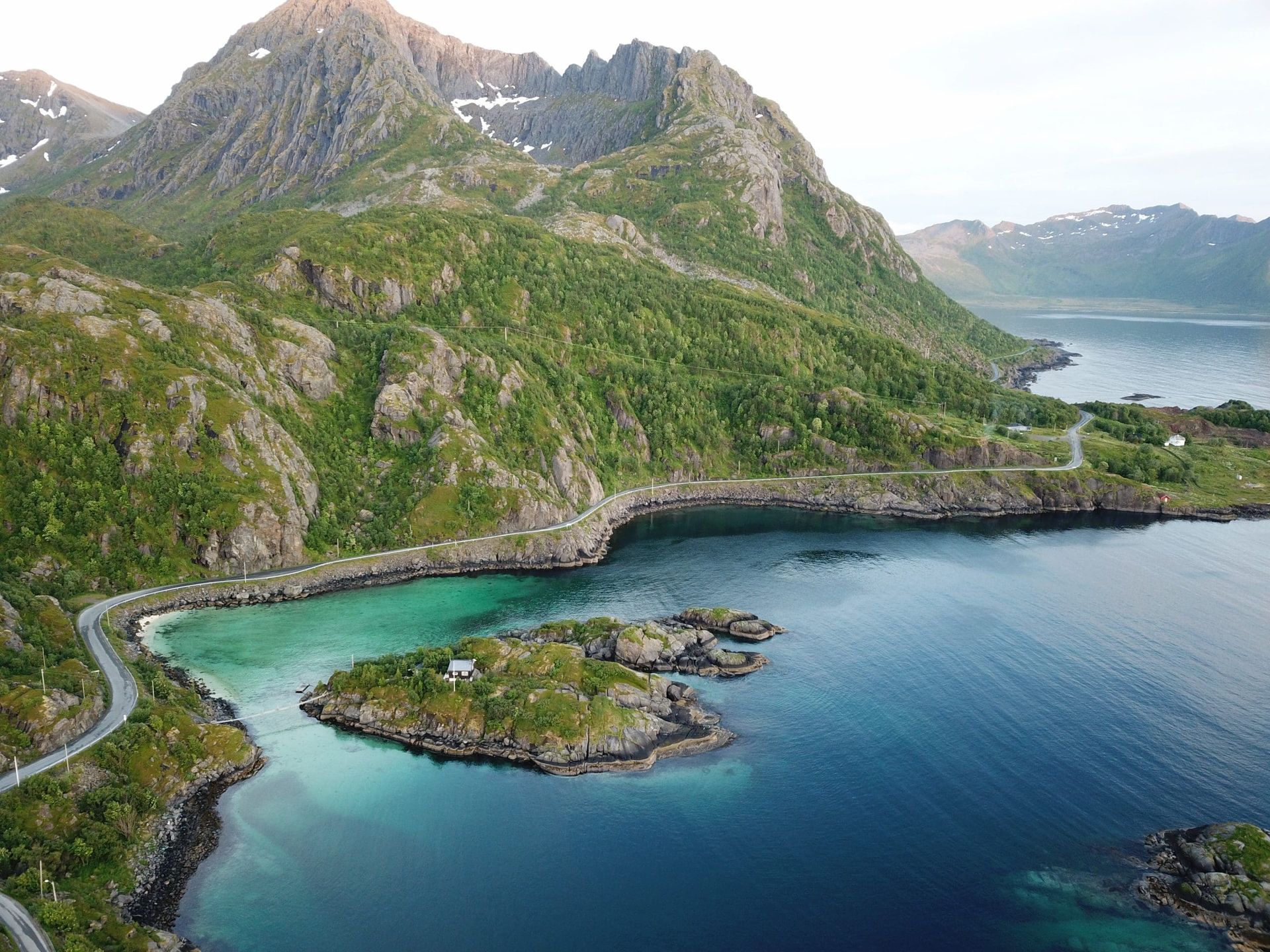 Coastal view of mountains and turquoise water with a road winding along the shoreline.